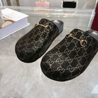 Gucci slide sandals with dark GG monogram fabric and gold horsebit hardware, rounded toe shape.