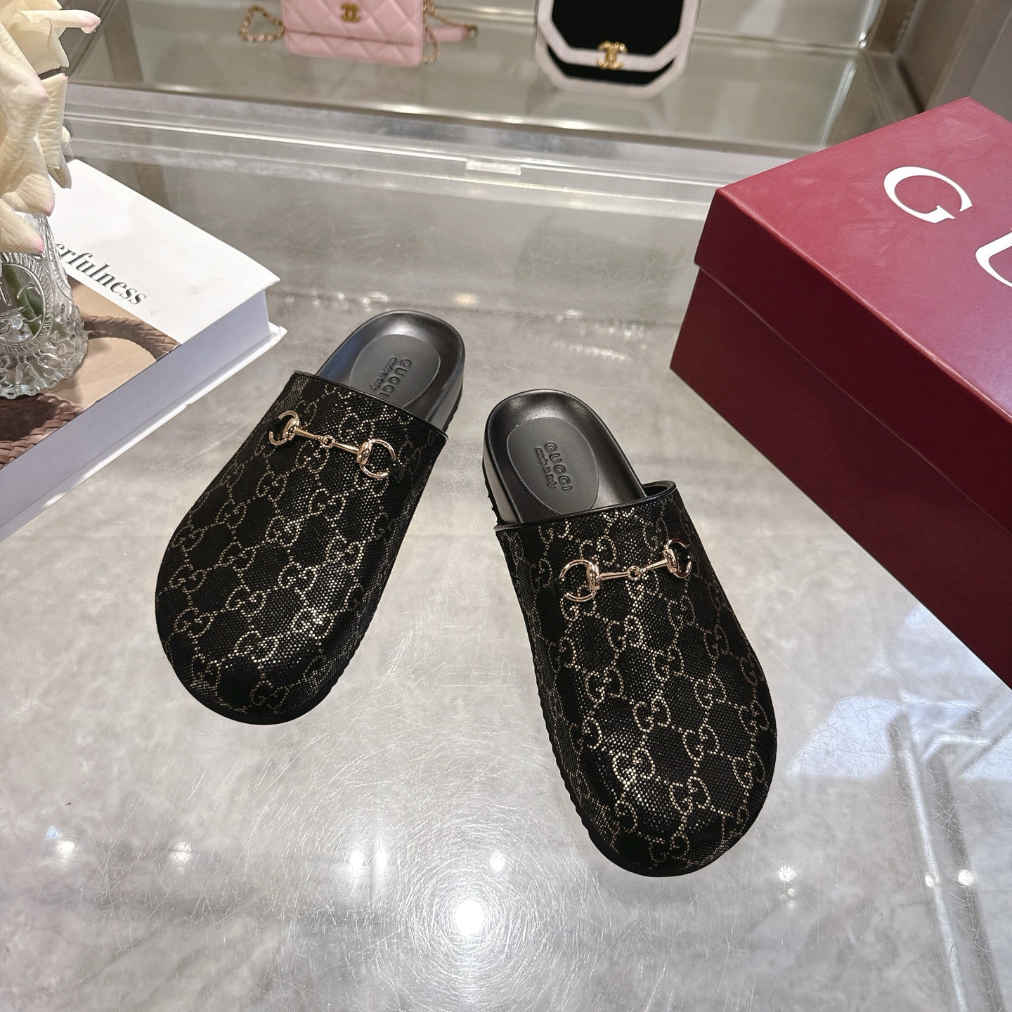 Gucci slide sandals showing front profile; dark GG monogram fabric with gold horsebit detail.