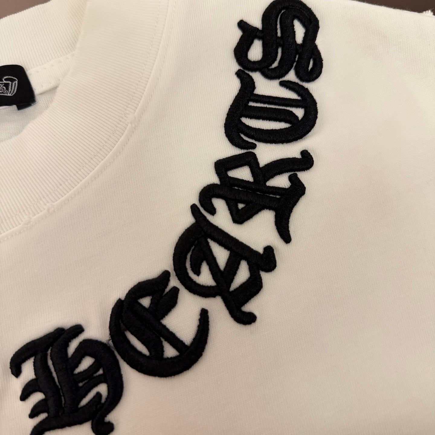 White T-shirt chest close-up with vertical black embroidered text