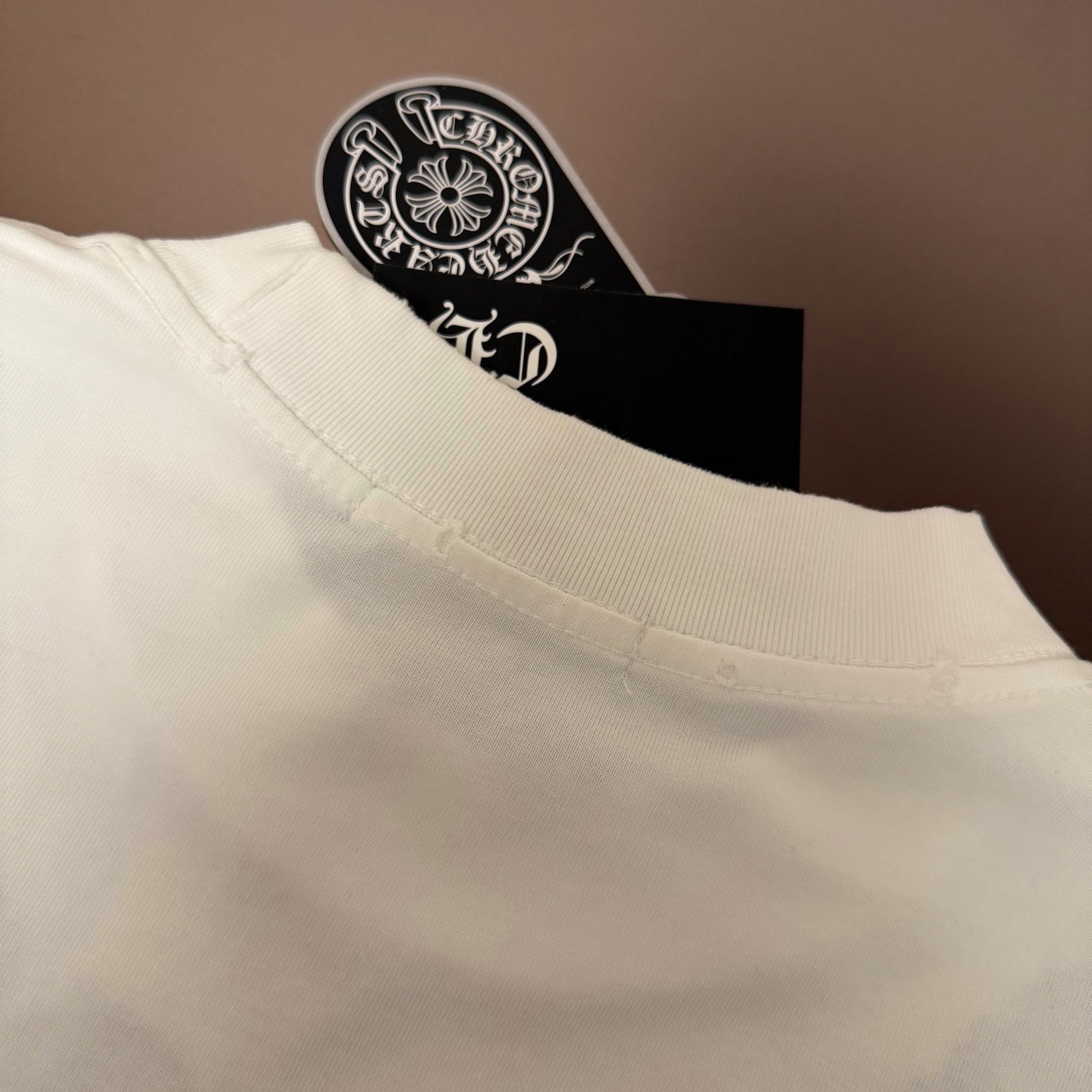 White T-shirt shoulder and neckline seam detail, with tag peeking