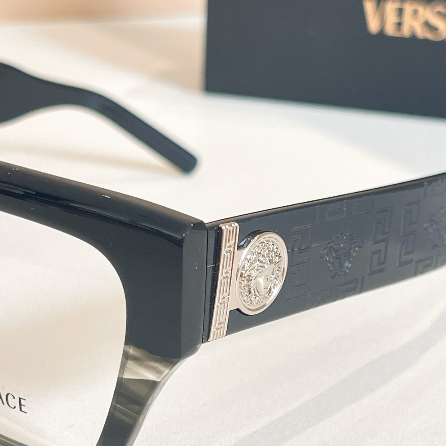 Eyeglasses frame close-up: dark temple with embossed pattern and gold emblem