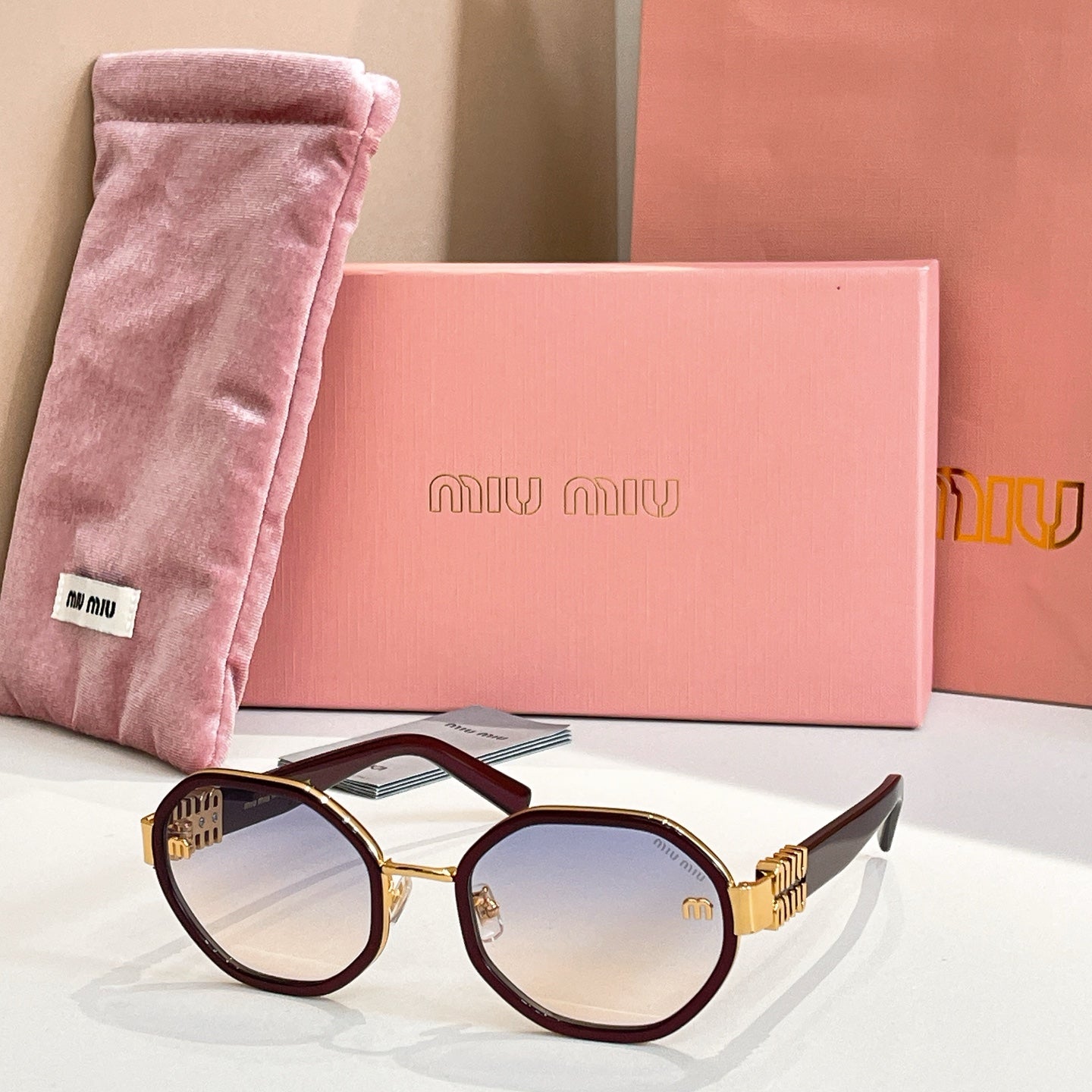 MiuMiu round sunglasses with dark maroon frames and gold-tone logo arms