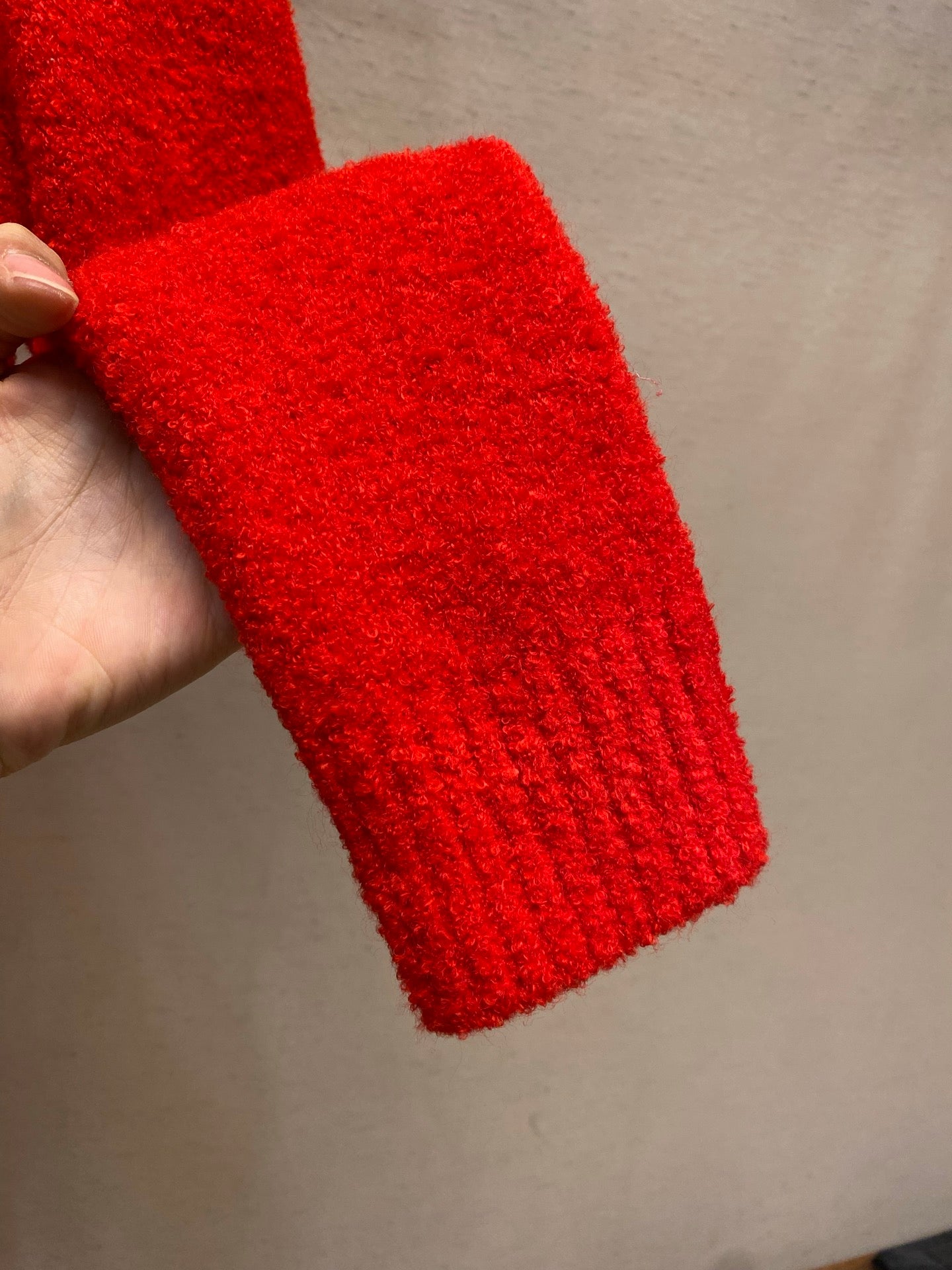 Red ribbed knit sweater sleeve cuff held in hand