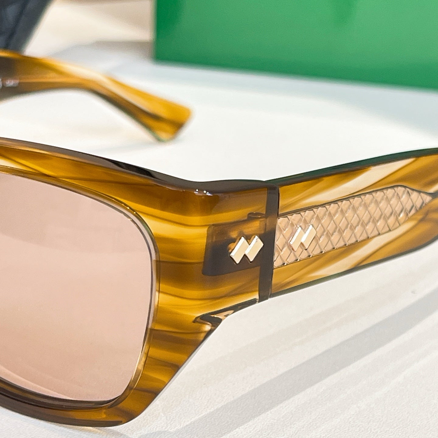 Close-up of amber sunglasses frame with gold-tone logo on temple
