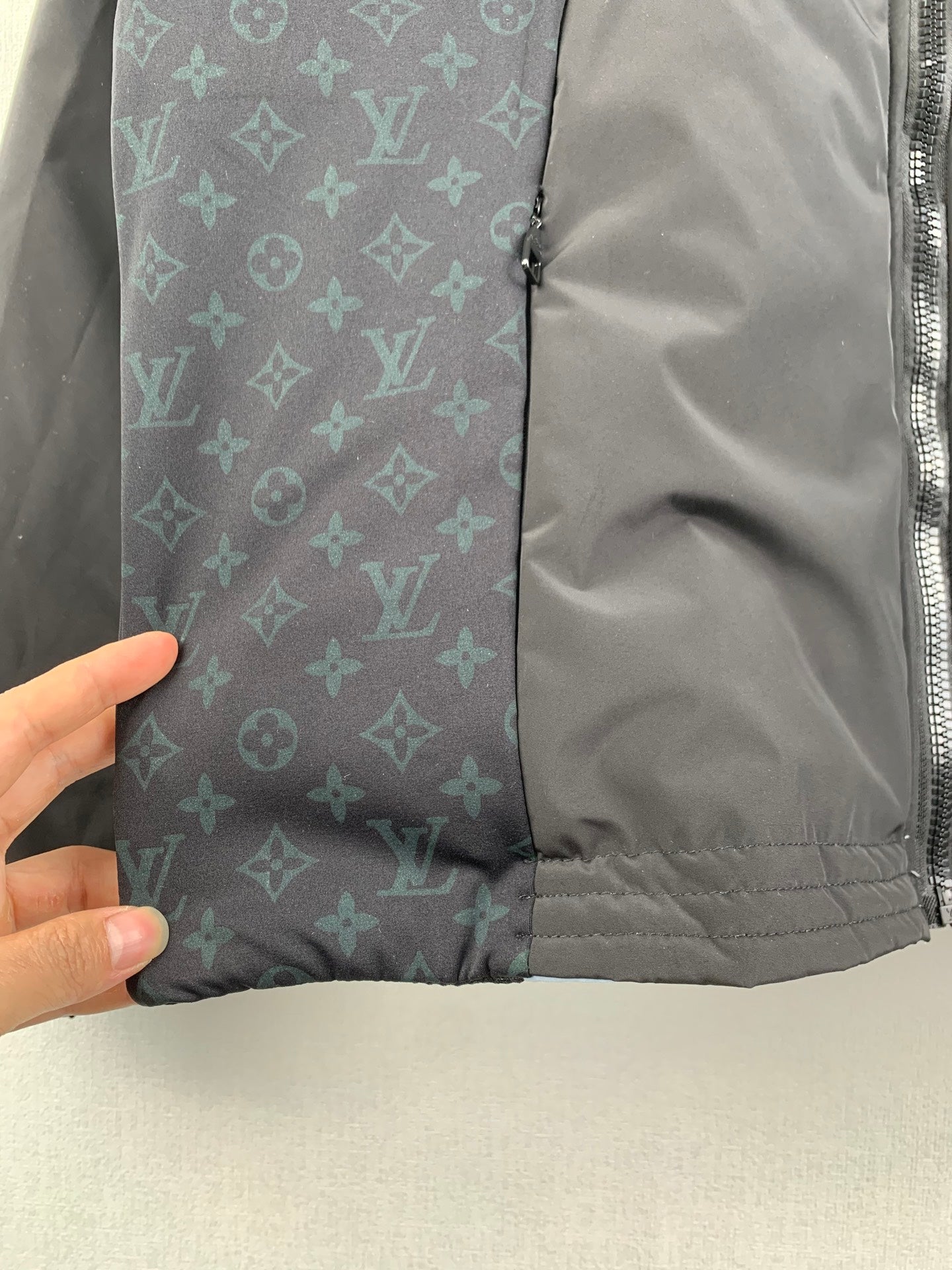 Dark gray jacket section with blue-green monogram panel and quilted hem.