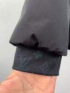 Hand holding dark gray jacket hem over blue-green monogram fabric.