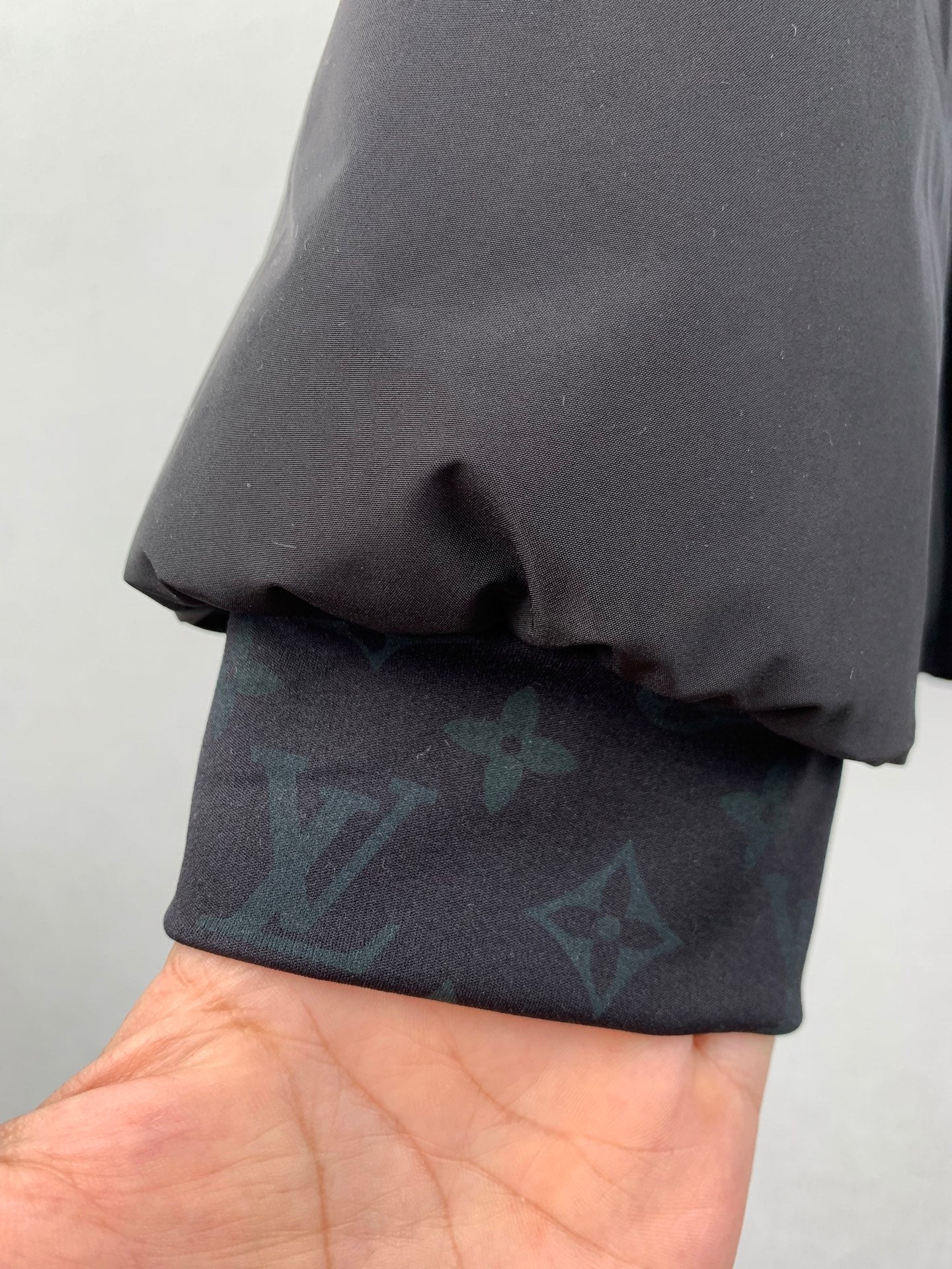 Hand holding dark gray jacket hem over blue-green monogram fabric.
