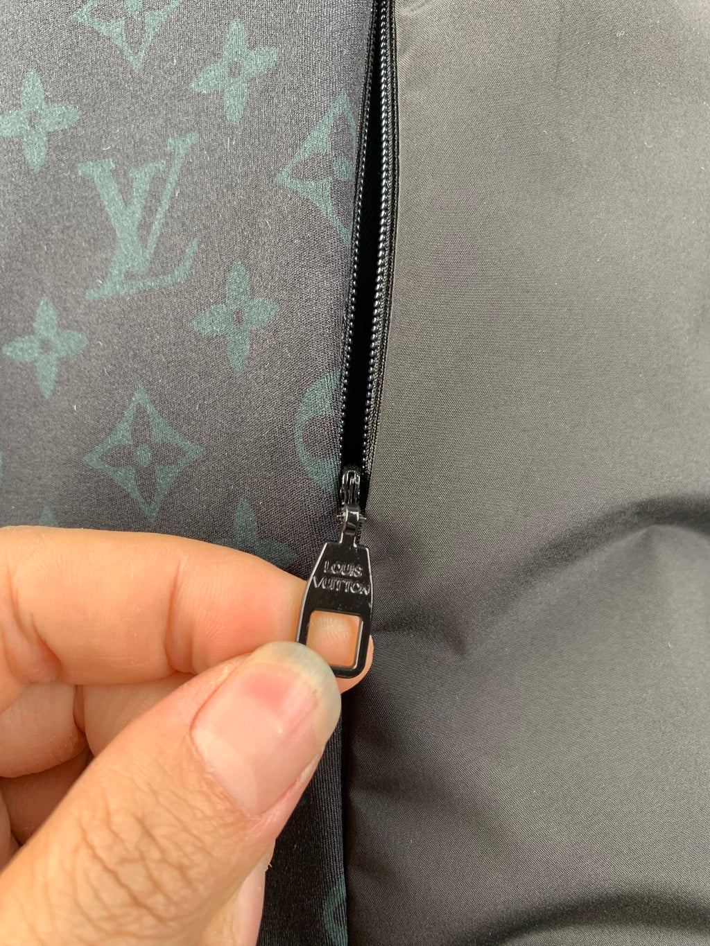 Close-up of jacket zipper and metal pull tab on monogram-lined fabric.