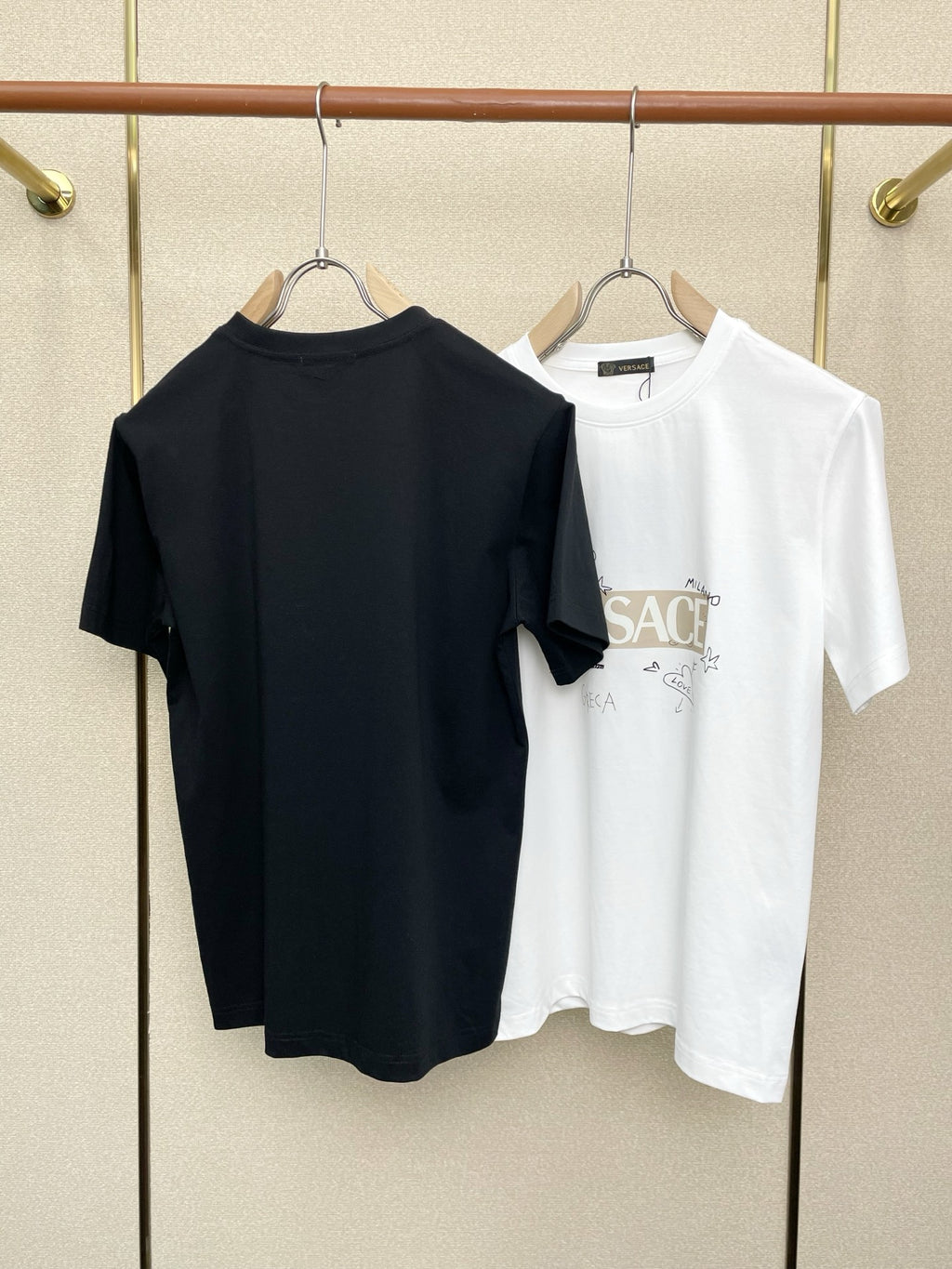 Black and white Versace graphic T-shirts on hangers, back view, crew neck.