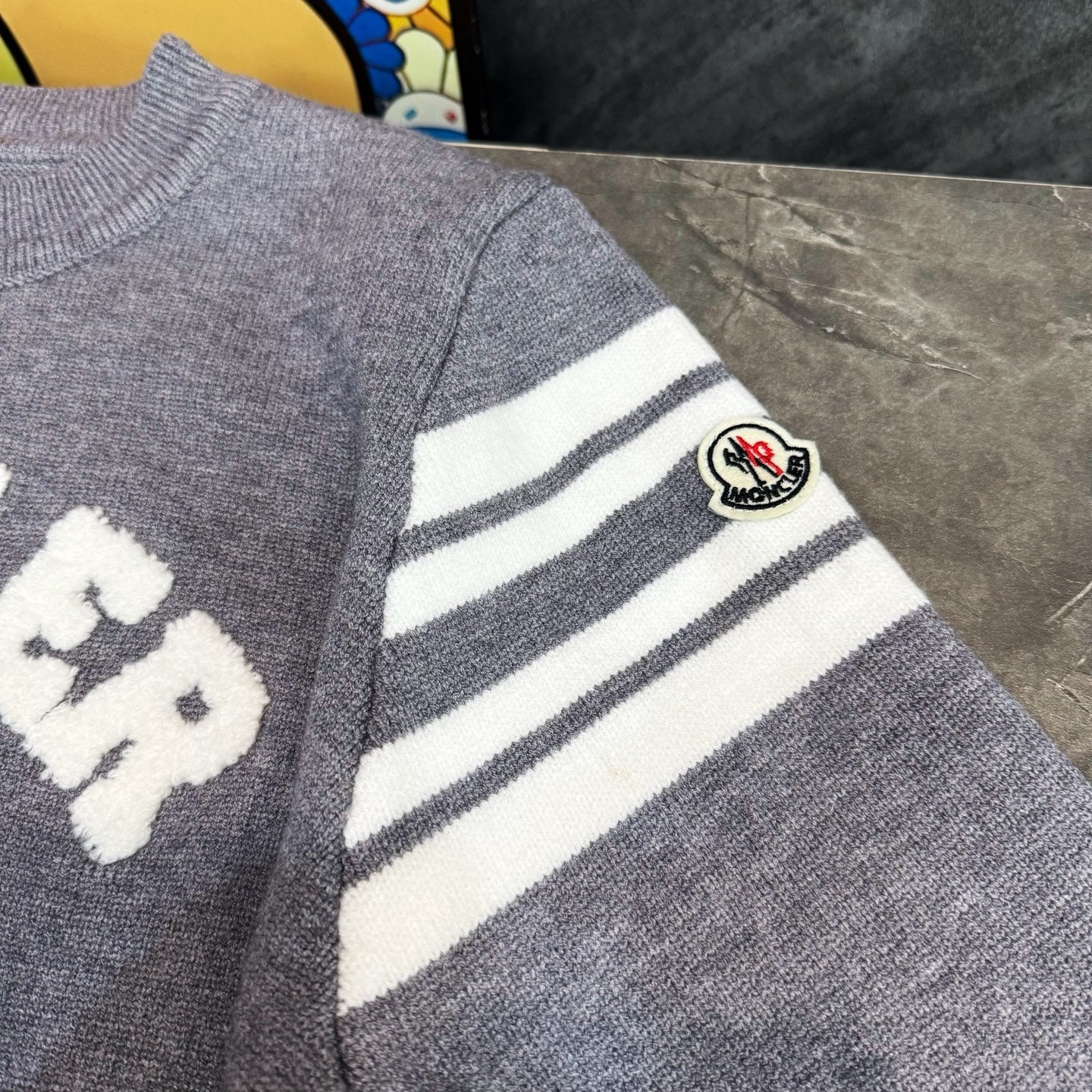 Light gray sweater sleeve with white striped panel and Moncler logo patch