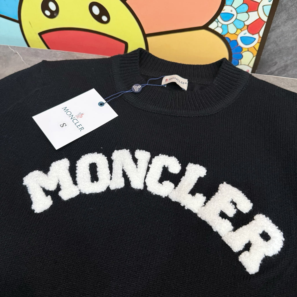 Black crewneck sweater with large white MONCLER letter graphic on the chest