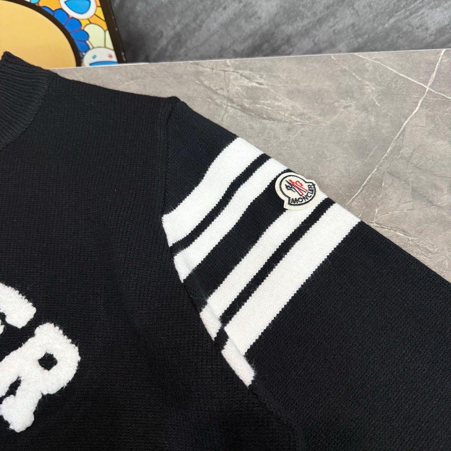 Black sweater sleeve with white striped cuff and Moncler logo patch