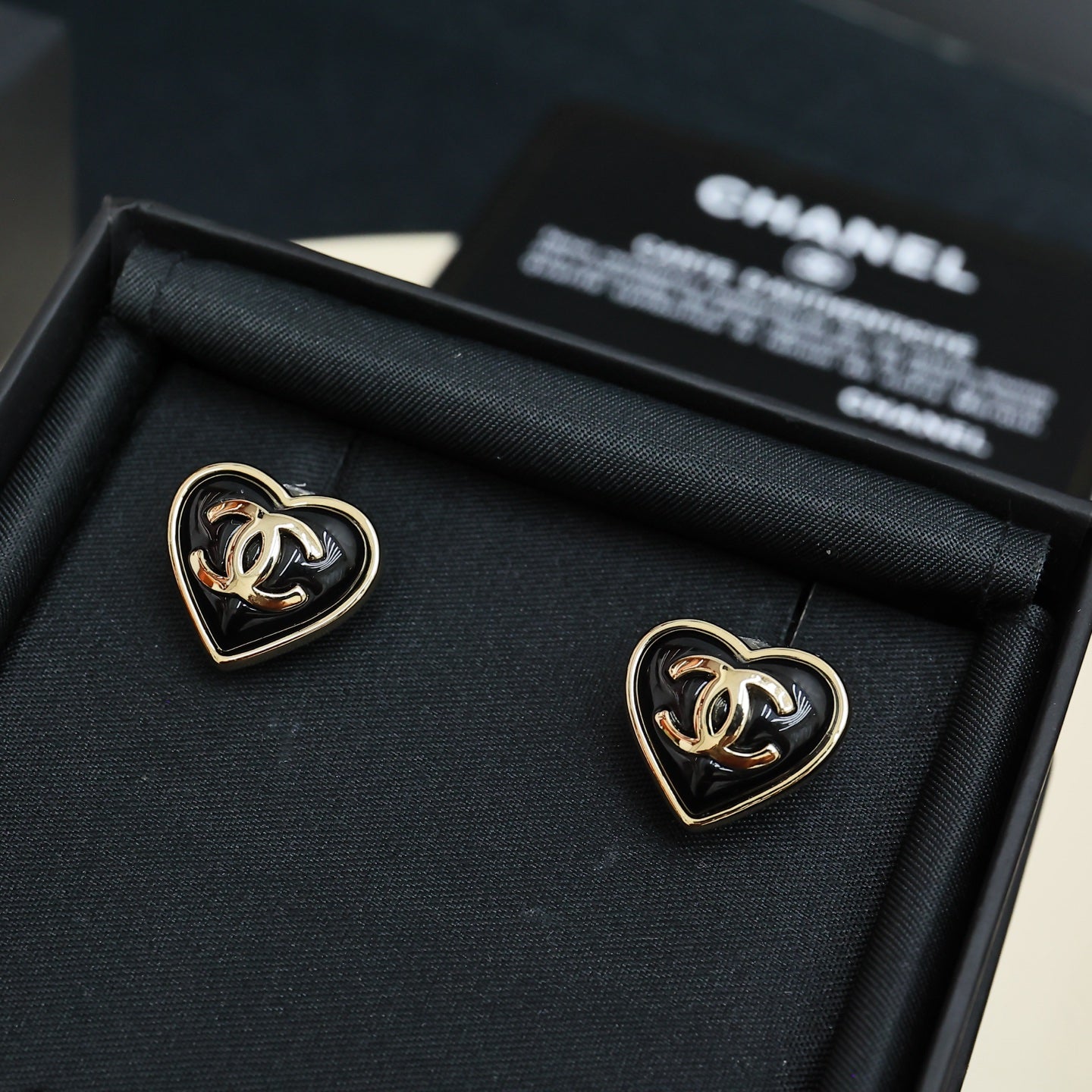 Heart-shaped Chanel stud earrings with gold trim and black enamel in display box