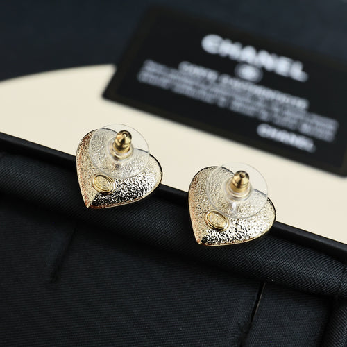 Heart-shaped Chanel stud earrings with gold-tone swirl and small gold emblem