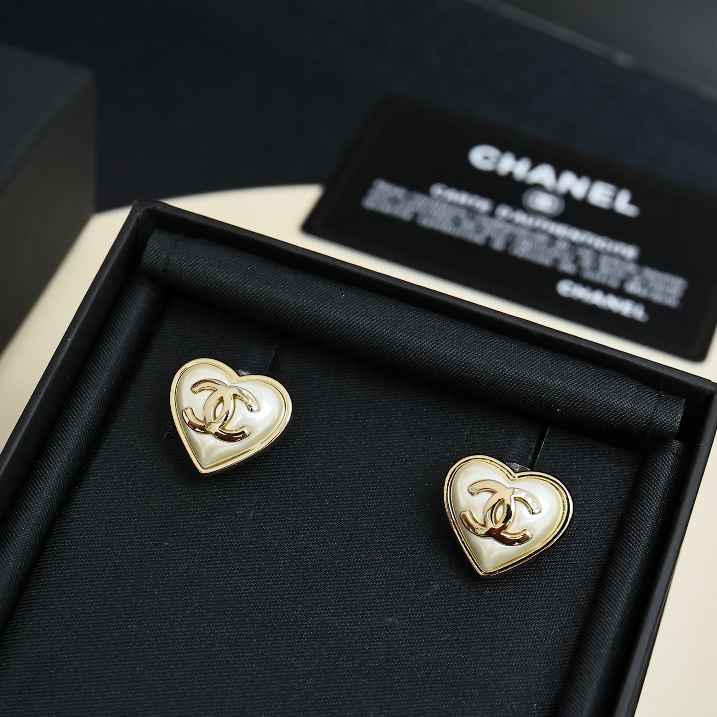 Heart-shaped Chanel stud earrings with white enamel and gold trim in display box