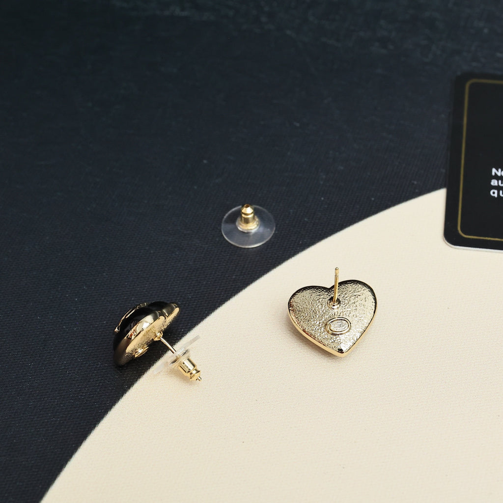 Heart-shaped Chanel stud earrings with double C logo on dark fabric