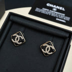 Pair of square logo stud earrings with black enamel and crystal details on dark display tray