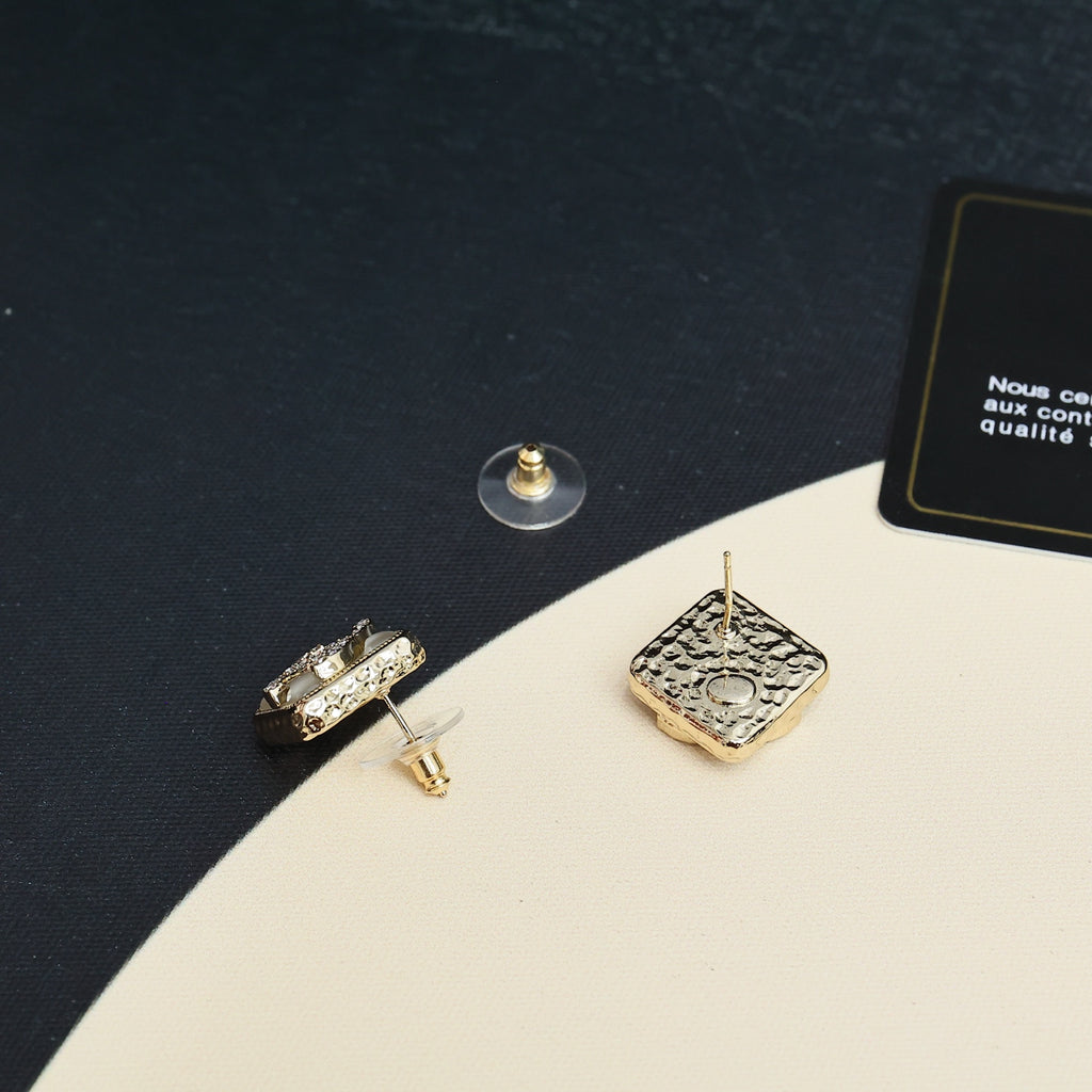 Square earrings with gold-tone posts and embellished logo backs on a dark surface