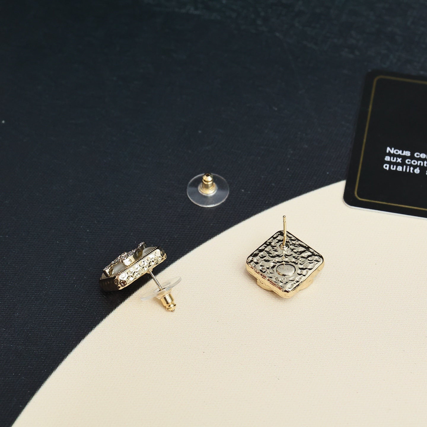 Square earrings with gold-tone posts and embellished logo backs on a dark surface