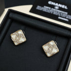Square stud earrings with white logo panel, gold-tone border, and sparkling crystal details