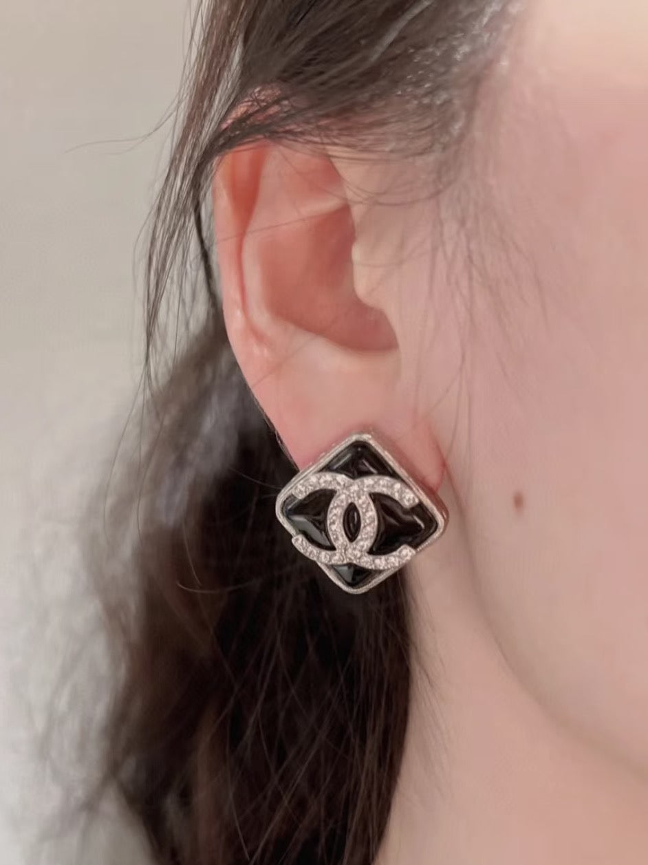 Square Chanel logo stud earring on ear with dark enamel surround and crystal accents