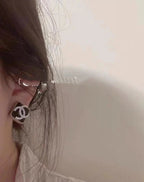 Logo stud earring near the ear with dark outline and small crystal embellishments