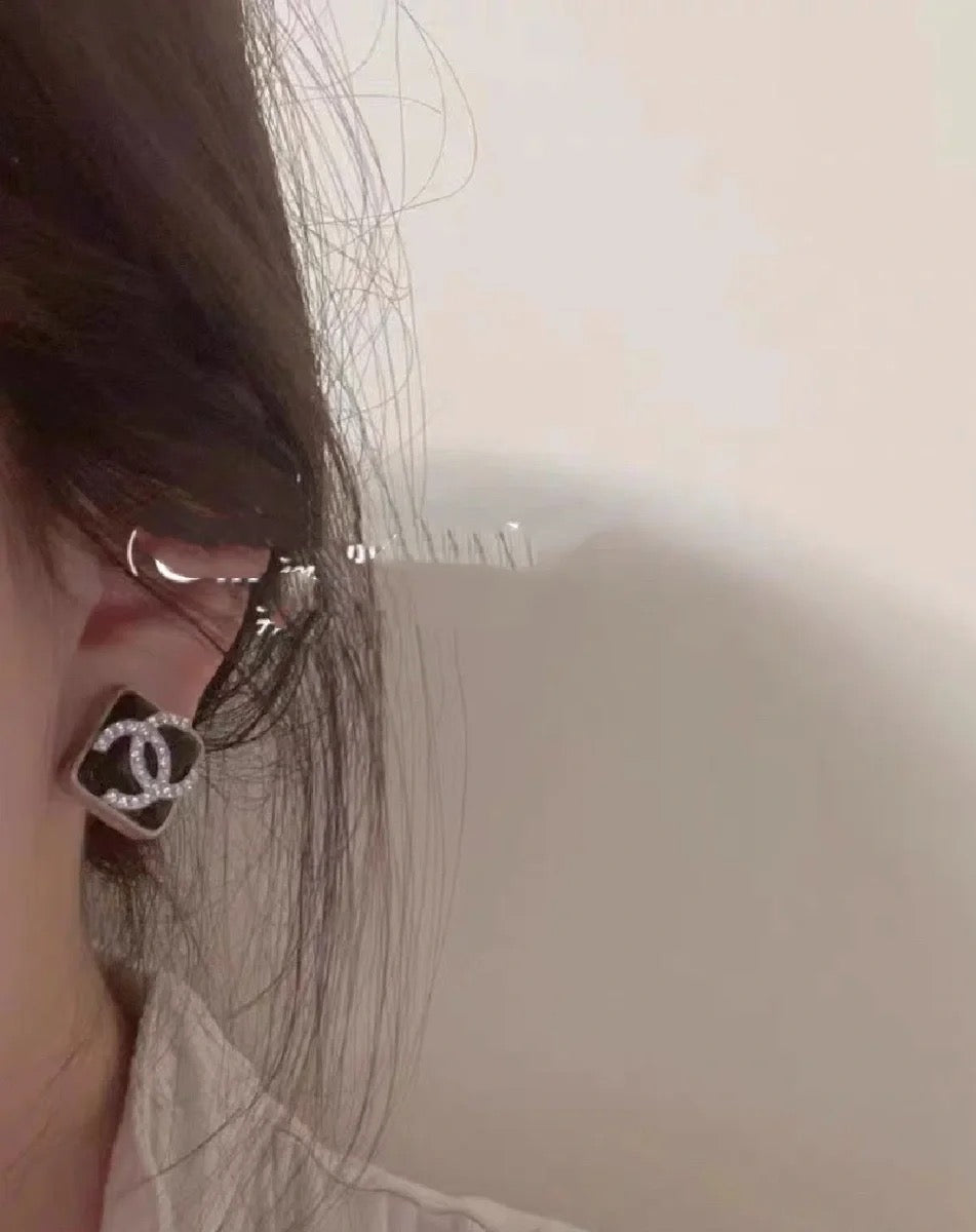 Logo stud earring near the ear with dark outline and small crystal embellishments