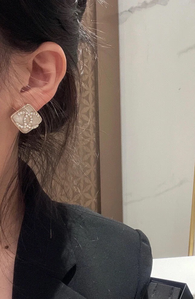 Square logo stud earring on the ear with sparkle stones and dark border details
