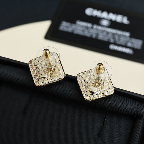 Square stud earrings with gold-tone posts and clear logo design on a dark base