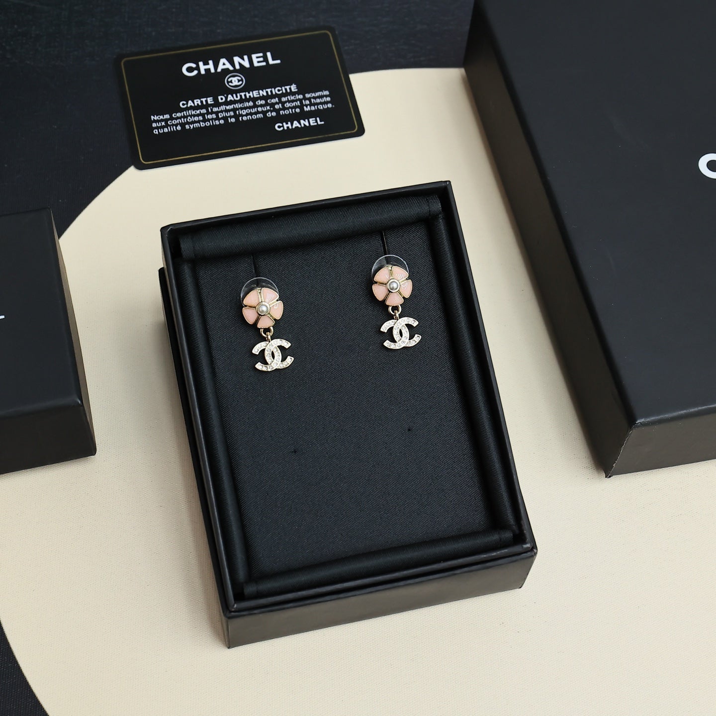 Chanel earrings displayed in black jewelry box, flower stud design with dangling CC logos