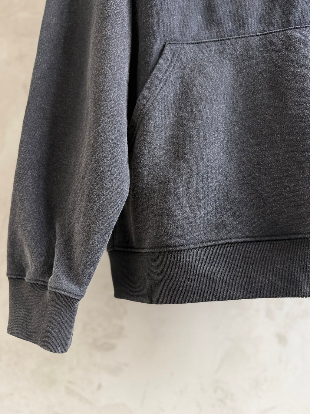 Dark gray hoodie sleeve and front pocket area, showing ribbed hem detail