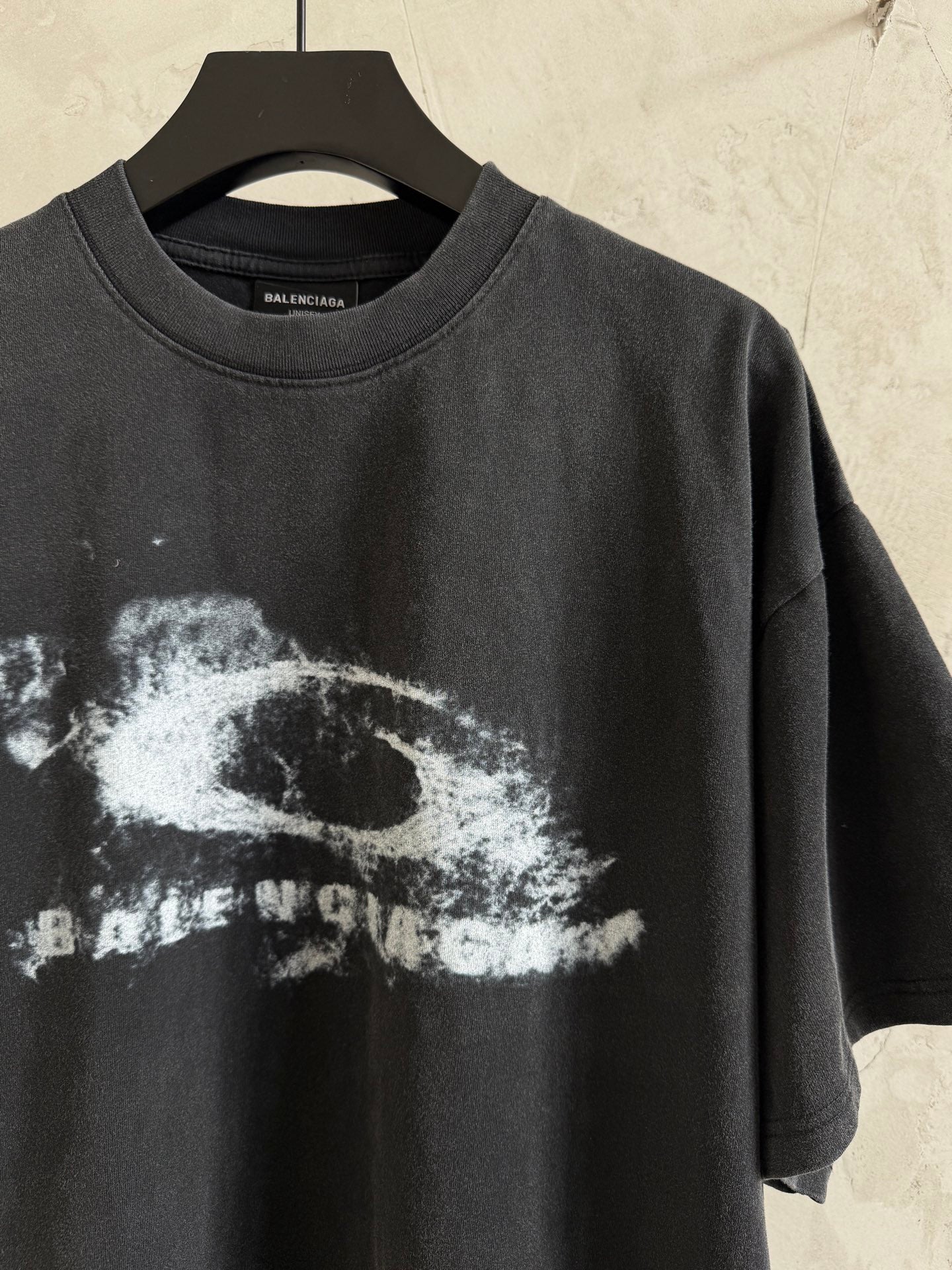 Balenciaga T-shirt close-up showing crewneck and white graphic print on dark gray fabric.