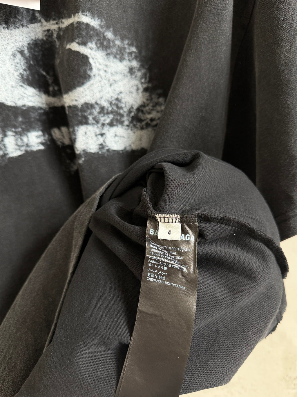 Balenciaga T-shirt close-up of neckline and fabric with care label on dark gray cloth.