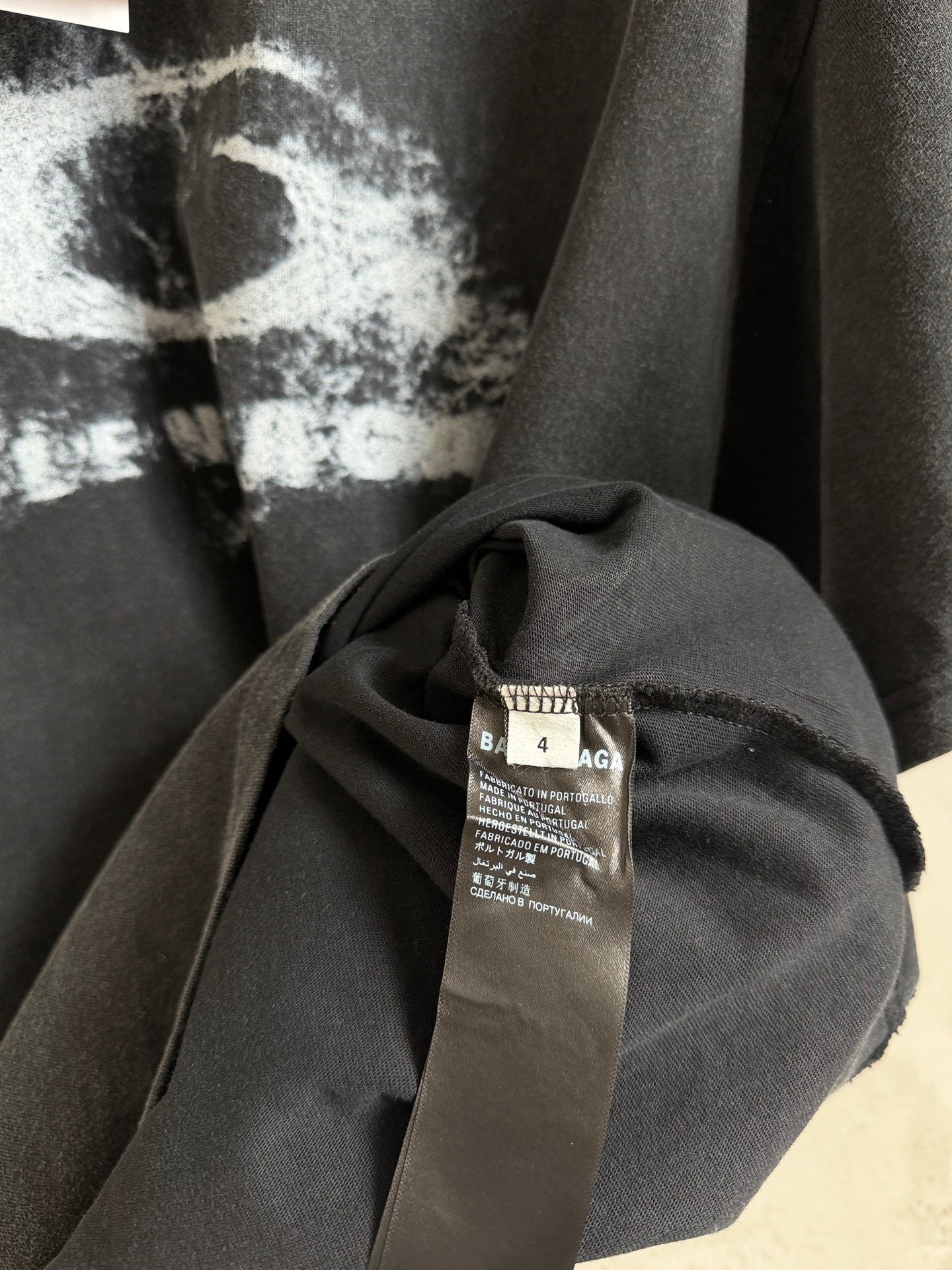 Balenciaga T-shirt close-up of neckline and fabric with care label on dark gray cloth.
