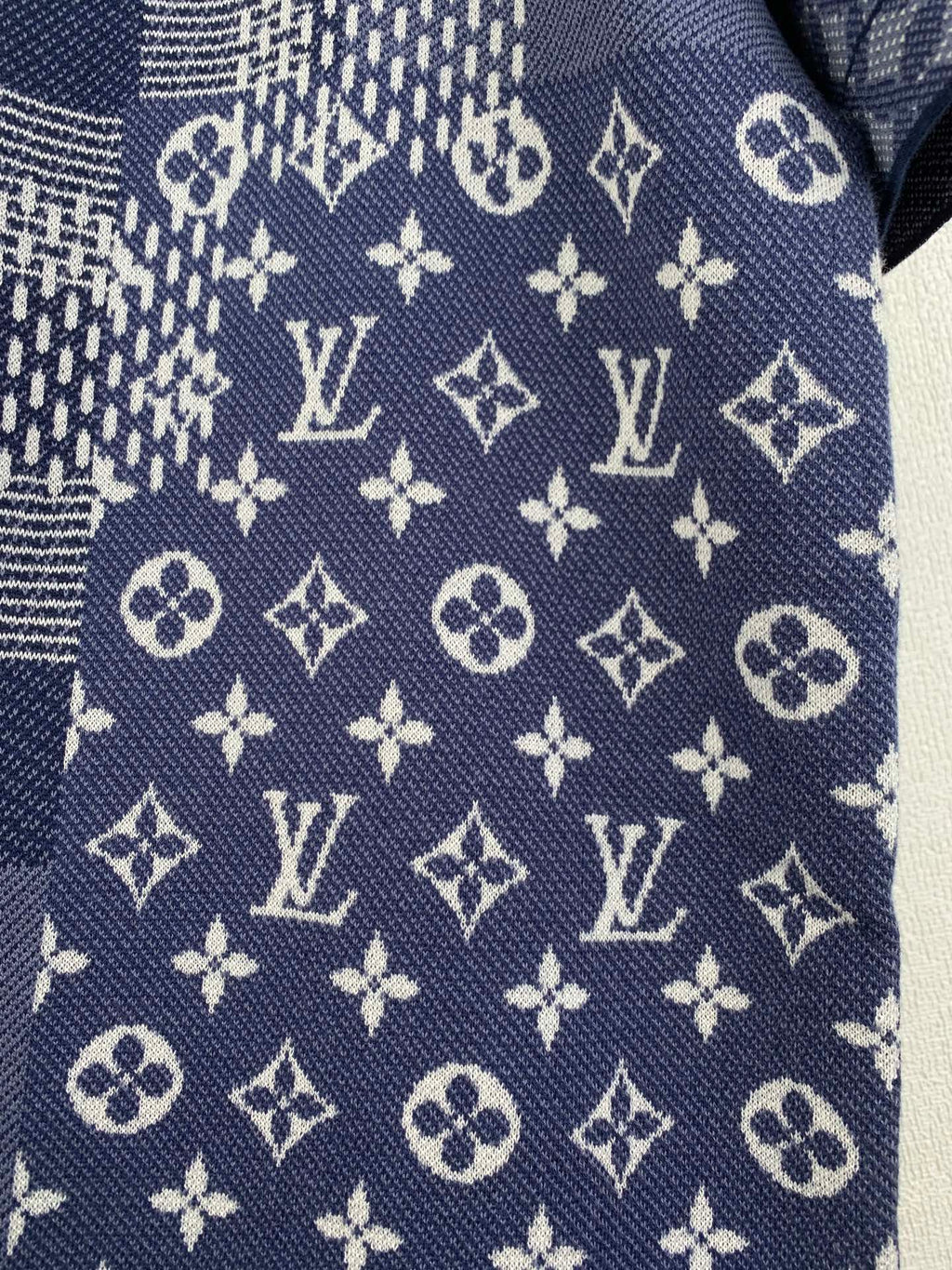 Navy blue short-sleeve fabric close-up with scattered monogram and cross motifs.