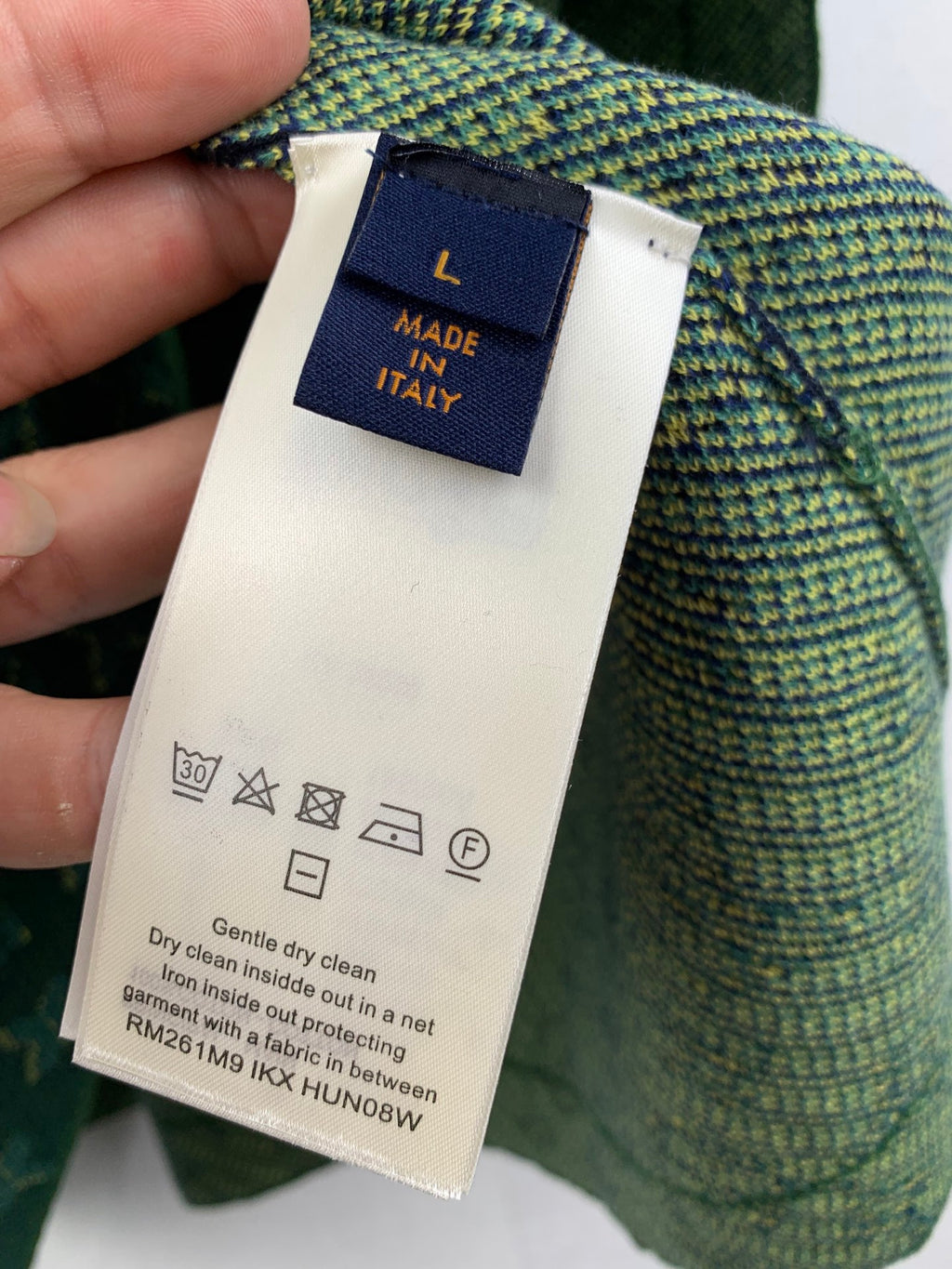 Louis Vuitton clothing label with Made in Italy and care symbols on green fabric.