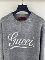 Gray knit crewneck sweater with Gucci script logo across the front