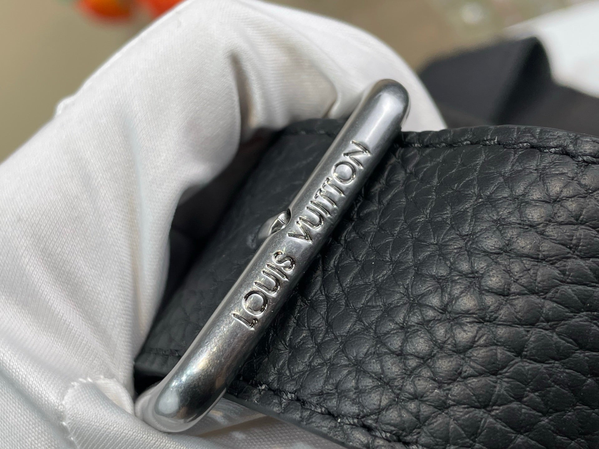 Louis Vuitton bag close-up of silver logo zipper pull on dark textured leather