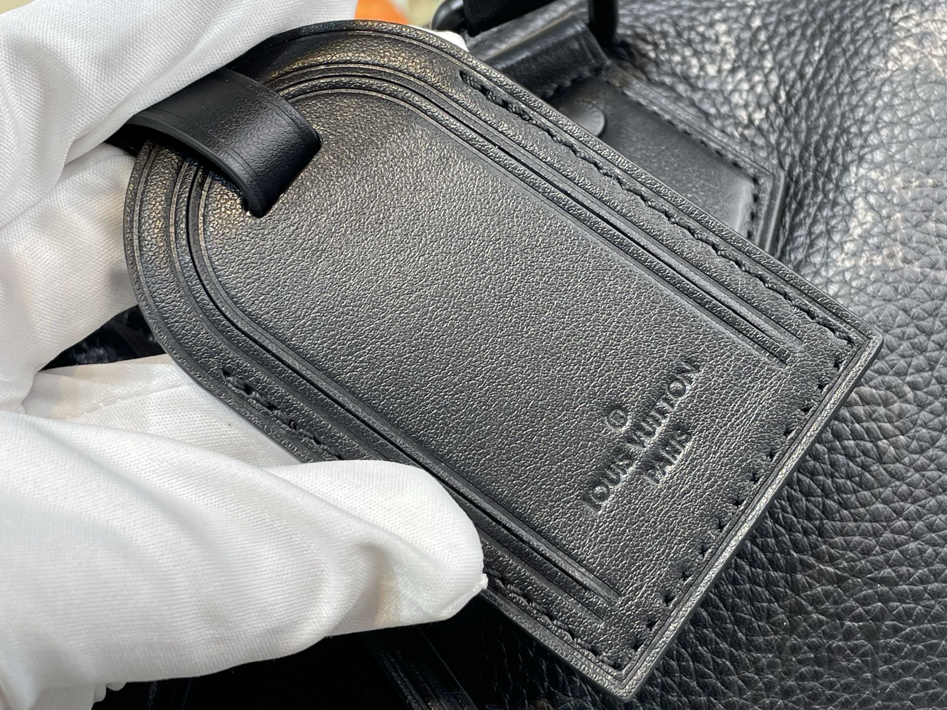 Black leather rectangular label with stitched edge and embossed logo on bag