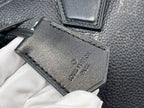 Black leather tag with debossed logo and stitched border on textured bag