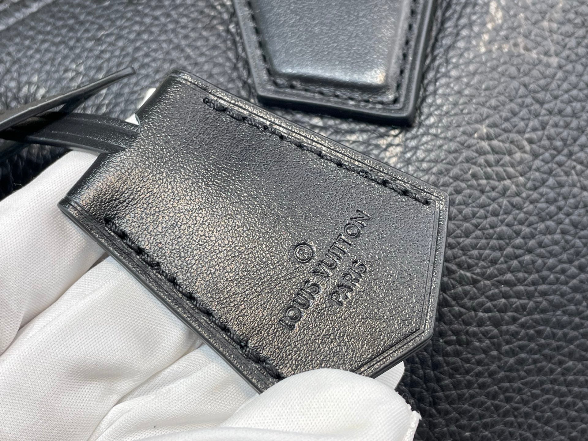 Black leather tag with debossed logo and stitched border on textured bag