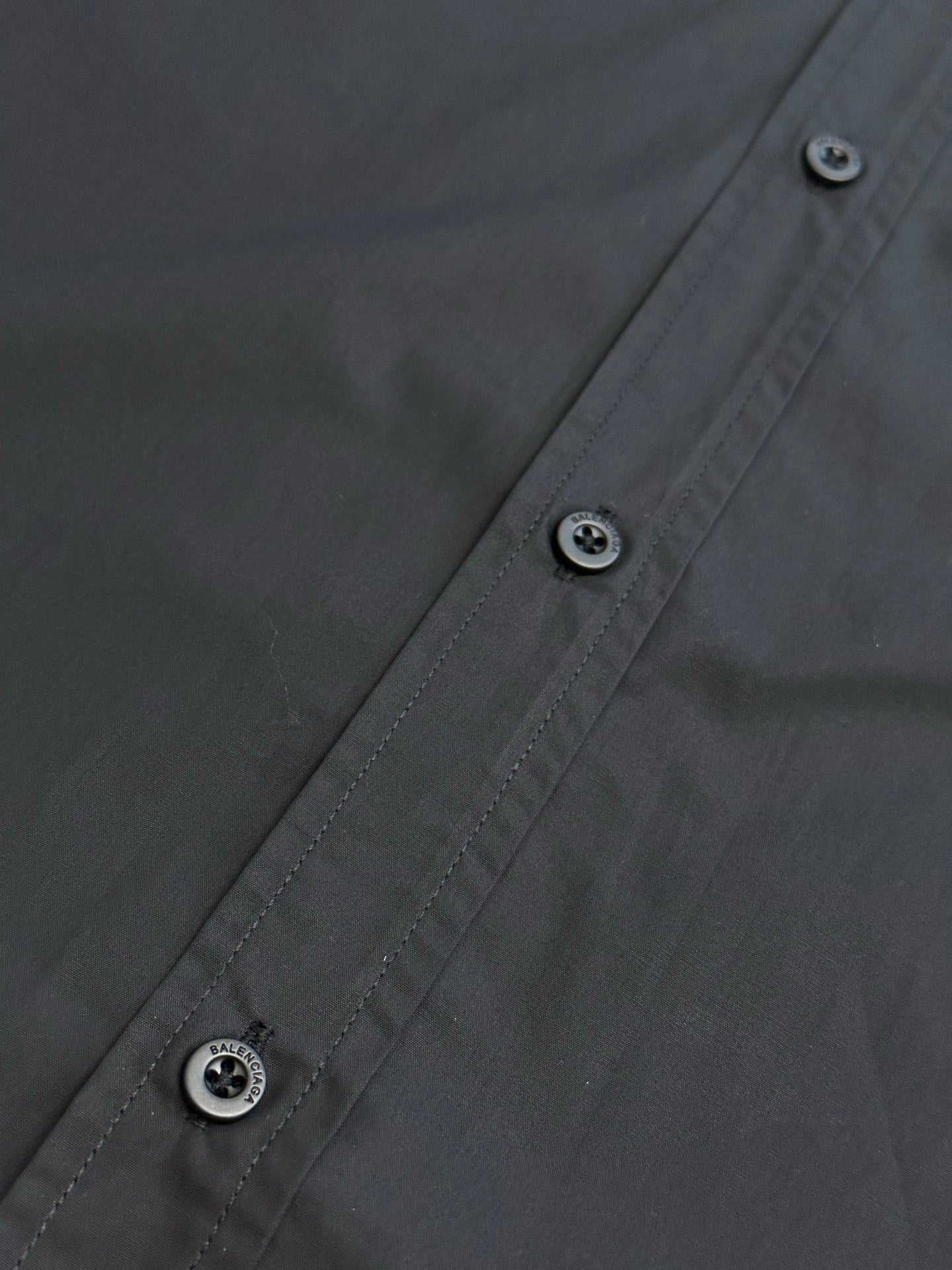 Dark charcoal button-up shirt front seam with two visible buttons and stitch lines