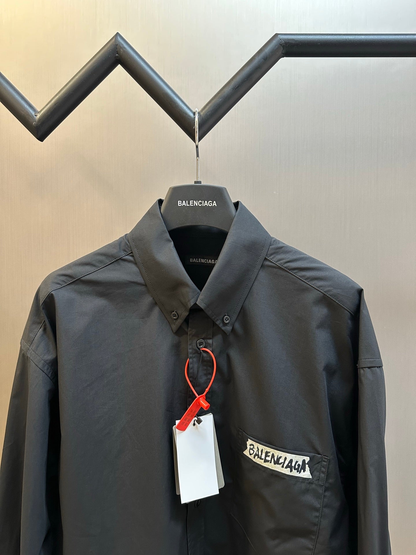Dark charcoal button-up shirt chest area with logo patch and hanging price tag