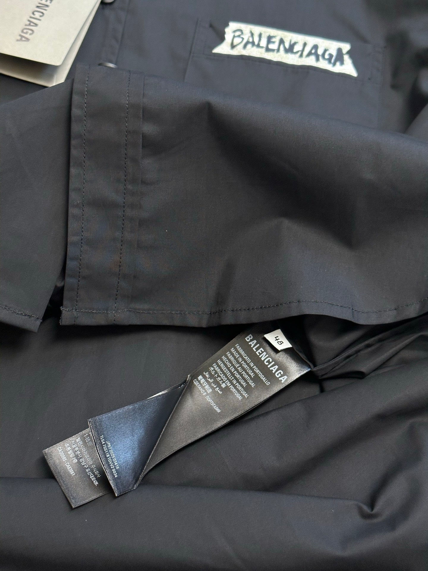 Dark charcoal button-up shirt front pocket with Balenciaga label and attached tags