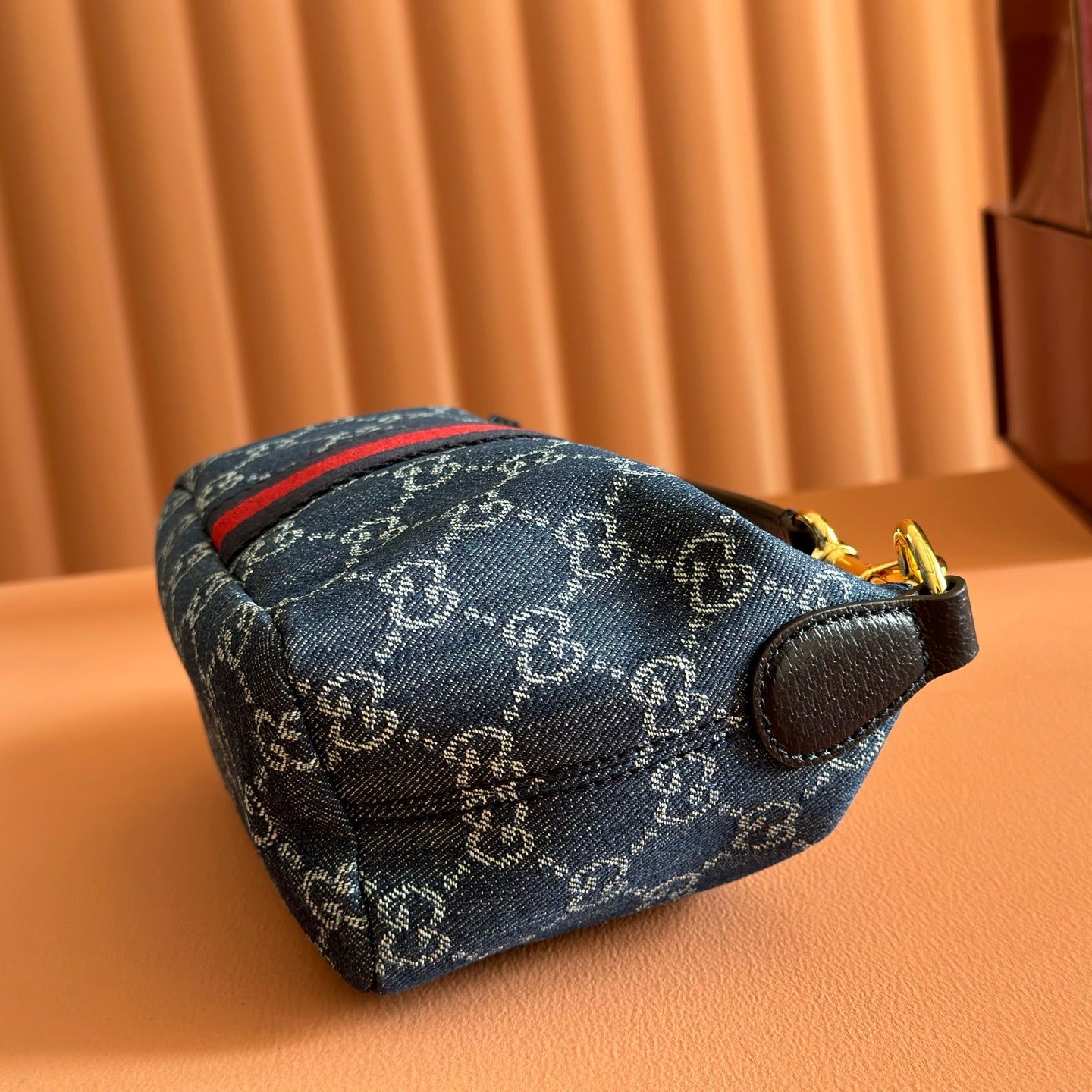 Gucci bag side view in blue GG canvas with red stripe and leather strap end