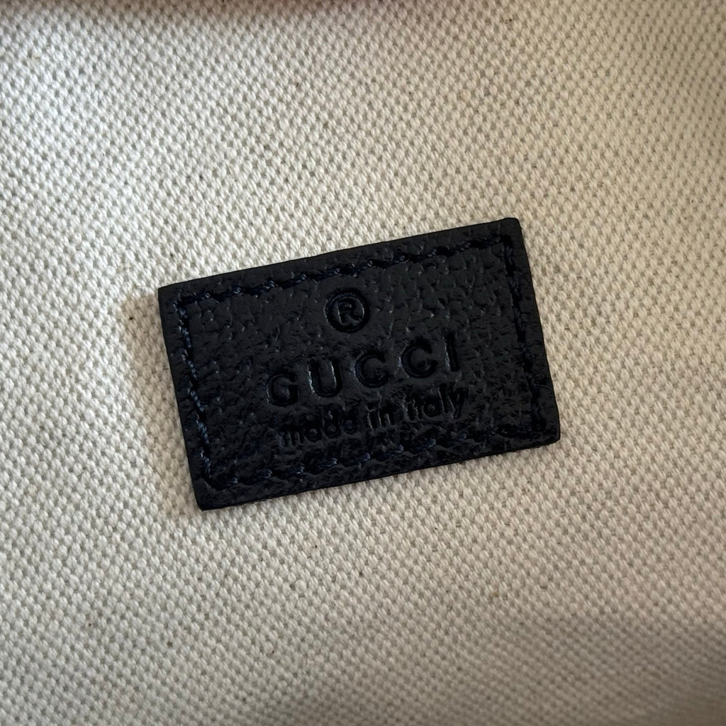 Gucci bag label: black embossed leather tag with Gucci text on beige lining.