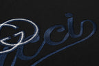 Close-up of blue Gucci script and heart emblem embroidery on black T-shirt