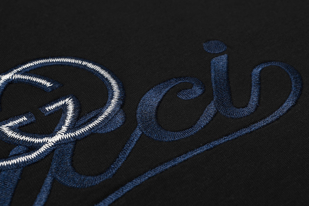 Close-up of blue Gucci script and heart emblem embroidery on black T-shirt