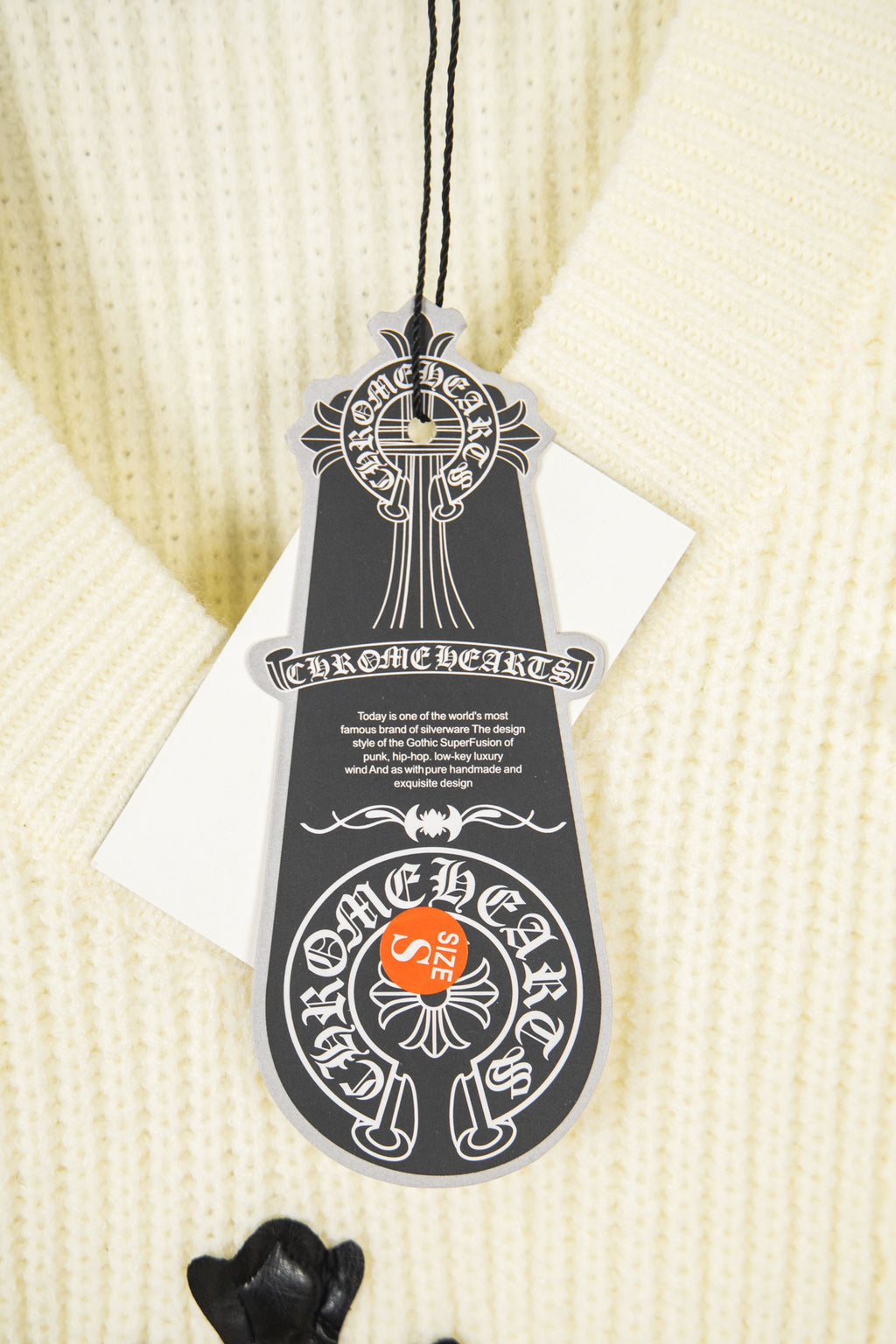 Off-white knit sweater with black logo hang tag and decorative cord