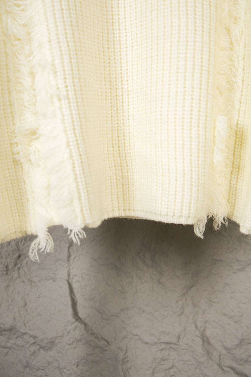 Off-white knit sweater hem with fringe edge and ribbed knit texture